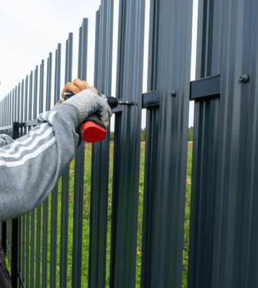 Monteur befestigt senkrechtes Aluminiumprofil mit Schrauben – Detailaufnahme vom Aufbau eines modernen Zauns. Polendeals.de